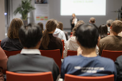 Programme director Elena Resch stands in front of a screen and welcomes the alumni, while students sit in the audience and listen.