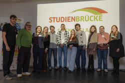 The participants in the Science Slam stand in front of a screen displaying the Studenbrücke logo.