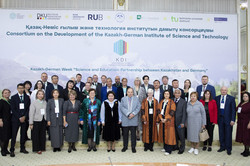 Group photo in front of a large poster with the words ‘Consortium on the Development of the Kazakh-German Institute of Science and Technology’