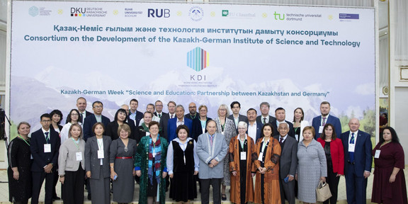 Gruppenfoto vor einem großen Plakat mit den Wörtern "Consortium on the Development of the Kazakh-German Institute of Science and Technology"