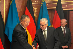 Zwei Männer schütteln die Hände. Hinter ihnen stehen deutsche und kasachische Flaggen.