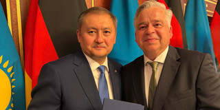 RUB-Kanzler Achim Dilling (rechts) und der kasachische Wissenschaftsminister Sayasat Nurbek. Hinter ihnen stehen deutsche und kasachische Flaggen.