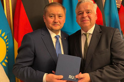 RUB-Kanzler Achim Dilling (rechts) und der kasachische Wissenschaftsminister Sayasat Nurbek. Hinter ihnen stehen deutsche und kasachische Flaggen.