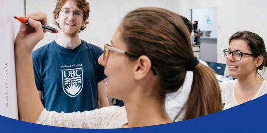 Several participants are standing around a whiteboard in a seminar room while one person writes down content with a marker and others watch attentively and discuss. The scene shows an interactive work situation during a Research Explorer Ruhr workshop.
