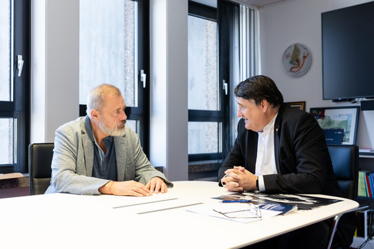 Nobel Peace Prize winner Dmitry Muratov in conversation with RUB Rector Martin Paul at a conference table. The two are sitting opposite each other in a bright office, with documents spread out on the table.