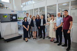 Eine Gruppe von zehn Personen steht in einem Forschungslabor der East Kazakhstan Technical University (EKTU). Links ist ein großes Laborgerät zu sehen, im Hintergrund befinden sich Glaswände, wissenschaftliche Geräte und ein anatomisches Skelettmodell. Die Gruppe blickt in die Kamera.