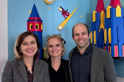 Drei Programmverantwörtliche stehen vor einem bunten Hintergrund und lächeln. 