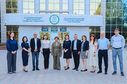Zehn Personen stehen vor dem Haupteingang der East Kazakhstan Technical University (EKTU). Über ihnen befindet sich das Universitätslogo sowie Beschriftungen in kasachischer und russischer Sprache. Die Gruppe posiert für ein gemeinsames Foto.