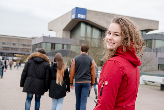 A student stands on the university bridge in front of the RUB and looks into the camera.