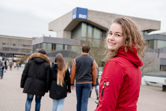 Eine Studentin steht an der Unibrücke vor der RUB und schaut in die Kamera.
